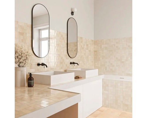 Helles modernes Badezimmer mit zwei weißen Keramik-Aufsatzwaschbecken, ovalen Spiegeln, schwarzen Armaturen und beigen quadratischen Wandfliesen.