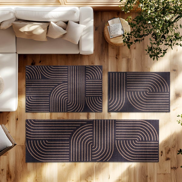 Draufsicht auf drei Teppiche mit geometrischem Bogenmuster auf einem Holzboden in einem hellen Wohnzimmer neben einem Sofa.
