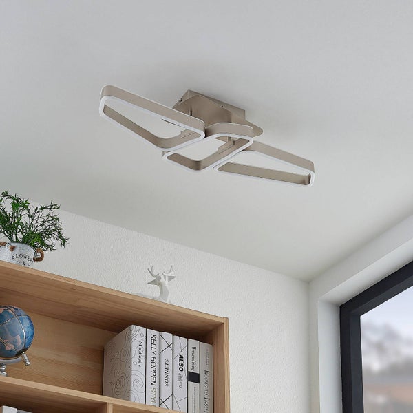 Moderne LED-Deckenleuchte mit drei ineinandergreifenden Rahmen aus Metall an der Zimmerdecke über einem Bücherregal aus Holz.