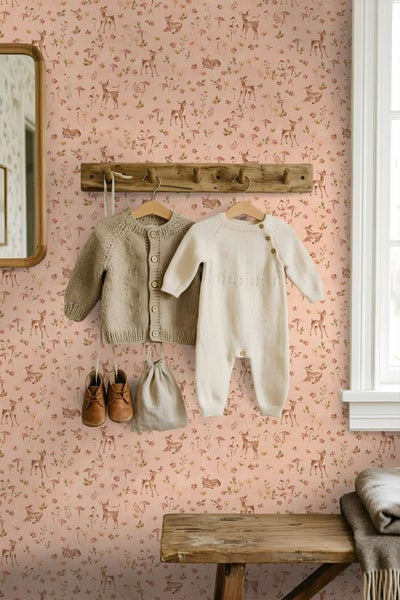 Kindertapete mit Waldmotiven und Rehen im Kinderzimmer mit einer hölzernen Garderobe und Babykleidung an der Wand.