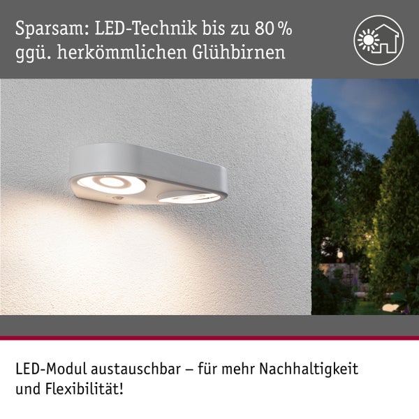 Moderne LED Außenwandleuchte mit zwei Lichtquellen an einer Wand, im Hintergrund ein Garten bei Nacht, energiesparend mit austauschbarem LED Modul.