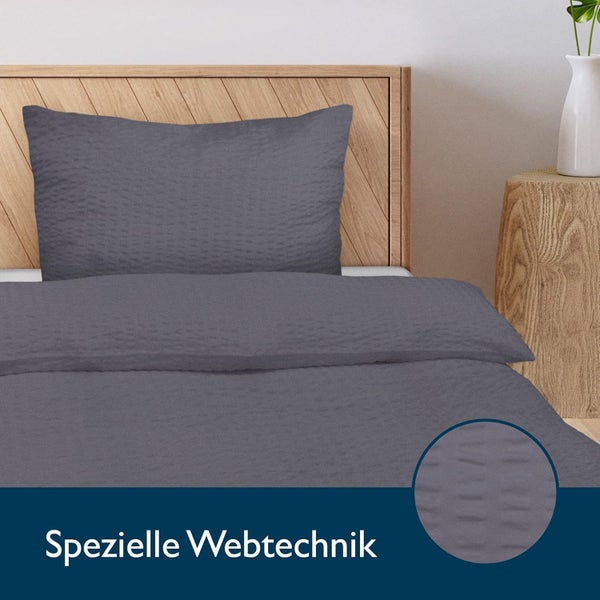 Graue Bettwäsche mit spezieller Webtechnik auf einem Holzbett mit passendem Kissen und strukturierter Oberfläche.