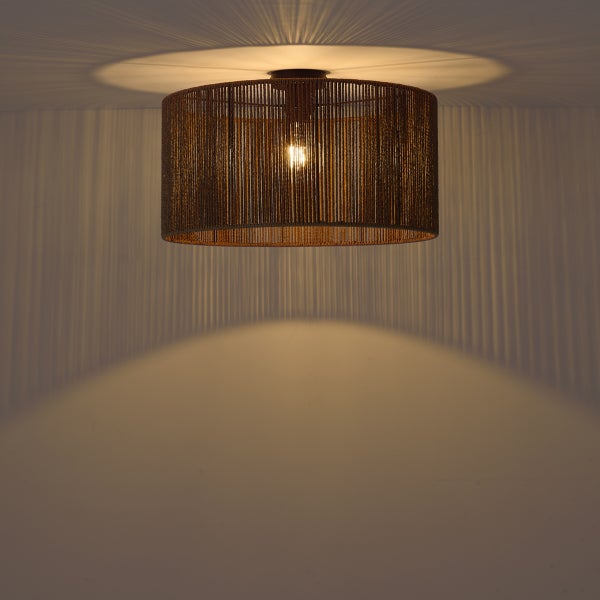 Eingeschaltete Deckenleuchte mit rundem Schirm aus braunen Schnüren wirft ein dekoratives Licht- und Schattenmuster an die Decke und Wand.