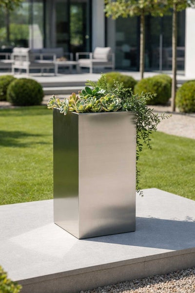 Hoher quadratischer Pflanzkübel aus gebürstetem Edelstahl mit Sukkulenten in einer modernen Gartenanlage.