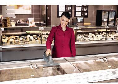 Eine Frau reinigt eine Kühltheke in einem Lebensmittelgeschäft mit einem Staubsauger.