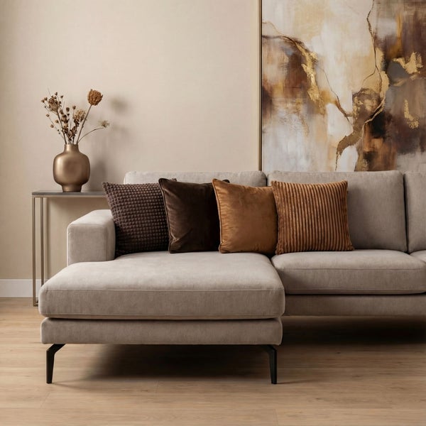 Modernes Wohnzimmer mit hellem Ecksofa, dekorativen Kissen in Brauntönen, abstraktem Wandbild und Vase mit Trockenblumen auf Parkettboden.