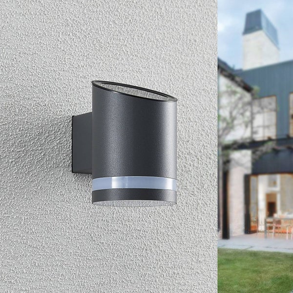 Schwarze zylindrische Solar-Außenwandleuchte mit schrägem Solarmodul und Lichtring an einer Hausfassade.