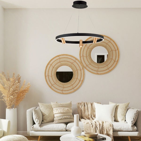 Moderne runde LED Pendelleuchte mit drei Strahlern über einem Sofa in einem hellen Wohnzimmer mit geflochtenen Wandspiegeln.