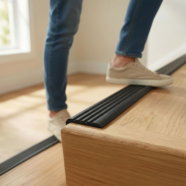 Eine Person steigt eine Treppe mit montiertem rutschhemmenden Treppenkantenprofil auf Holzstufen hinauf.
