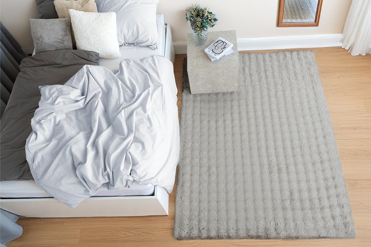 Heller Hochflor-Teppich mit Streifenmuster vor einem Bett in einem modern eingerichteten Schlafzimmer mit Holzboden und Beistelltisch.