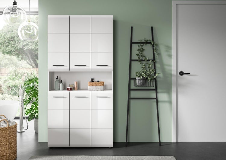 Moderner Badezimmer-Hochschrank in Weiß-Hochglanz mit schwarzen Griffen und offenem Fach in einem hellen Badezimmer mit Dekoleiter und Pflanze.