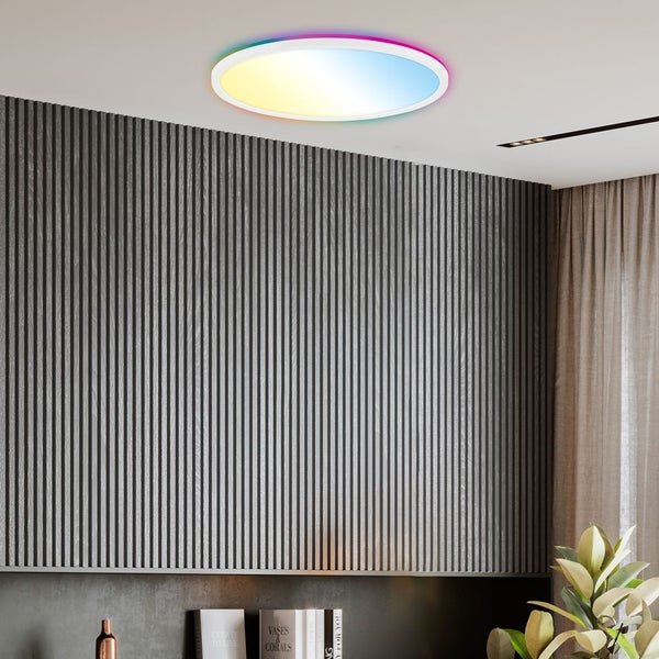 Moderne runde Deckenleuchte mit farbigem Licht an weißer Zimmerdecke in modernem Raum mit dunkler Lamellenwand und Bücherregal.