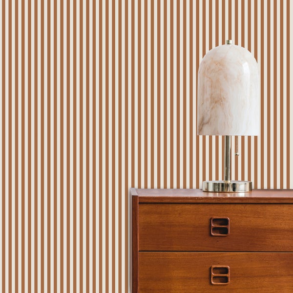 Gestreifte Tapete mit schmalen vertikalen Streifen an einer Wand hinter einer hölzernen Kommode mit einer Lampe in Marmoroptik.