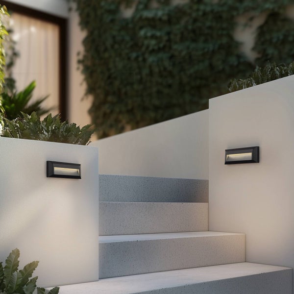 Zwei schwarze, rechteckige Außenwandleuchten an hellen Gartenmauern beleuchten eine Treppe aus Stein.