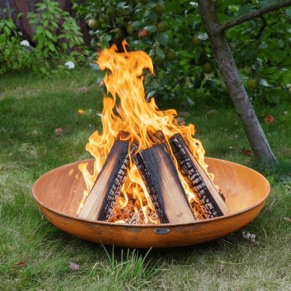 Brennende Holzscheite in einer metallenen Feuerschale im Garten auf dem Rasen.