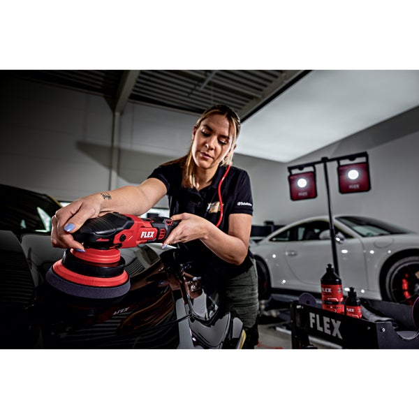 Eine Person poliert mit einer akkubetriebenen Exzenterpoliermaschine von FLEX die Motorhaube eines schwarzen Autos in einer Werkstatt.
