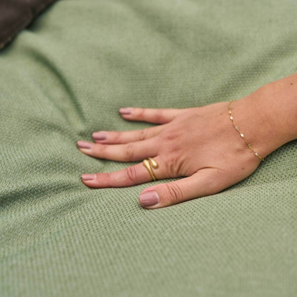 Hand auf einem grünen Kissen mit gewebter Struktur.