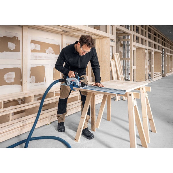 Handwerker schneidet eine Holzplatte mit einer Bosch Handkreissäge, Führungsschiene und Staubabsaugung auf Sägeböcken in einer Werkstatt.