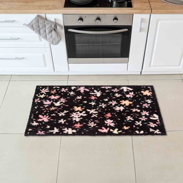 Küchenszene mit einer schwarzen Fußmatte mit Blumenmuster vor einer Küchenzeile.