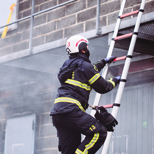 Feuerwehrmann in Schutzkleidung auf einer Teleskopleiter aus Aluminium an einem Gebäude.