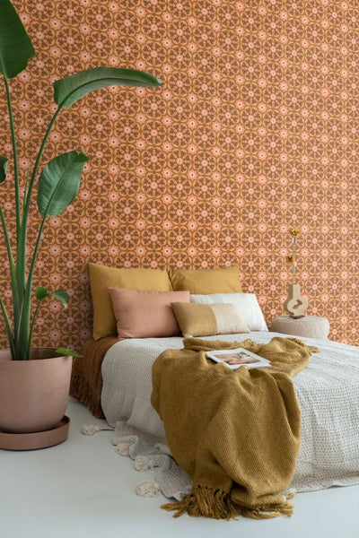 Schlafzimmer mit Vliestapete im Retro-Design, Bett mit Kissen und Decken, große Zimmerpflanze im Topf.