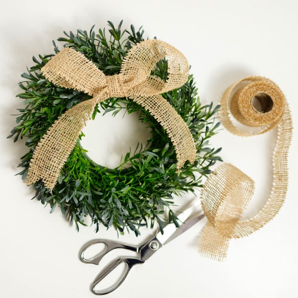 Grüner Kranz mit Schleife aus Jute, Rolle mit Juteband und eine Schere.