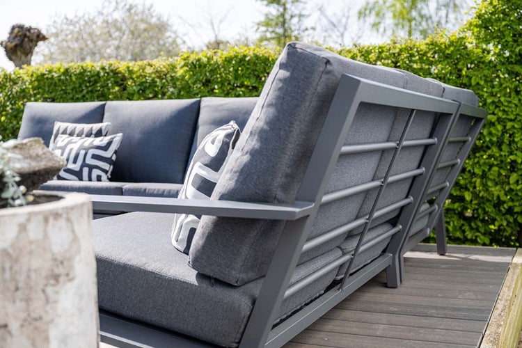 Moderne Garten-Lounge-Ecke mit anthrazitfarbenem Aluminiumgestell, dunklen Sitzkissen und gemusterten Zierkissen auf einer Holzterrasse.