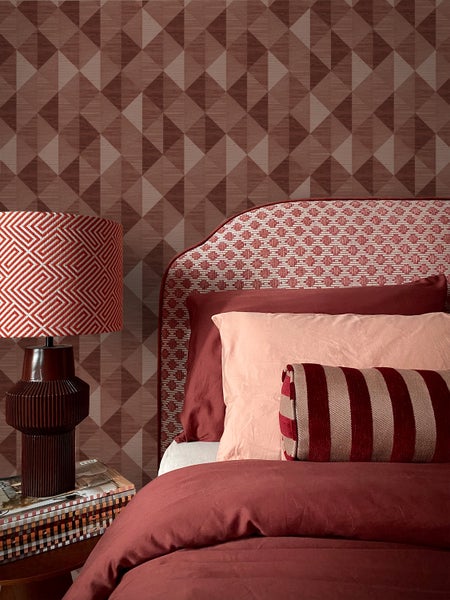 Vliestapete mit geometrischem Dreiecksmuster in einem Schlafzimmer mit Bett und gemusterter Tischleuchte.