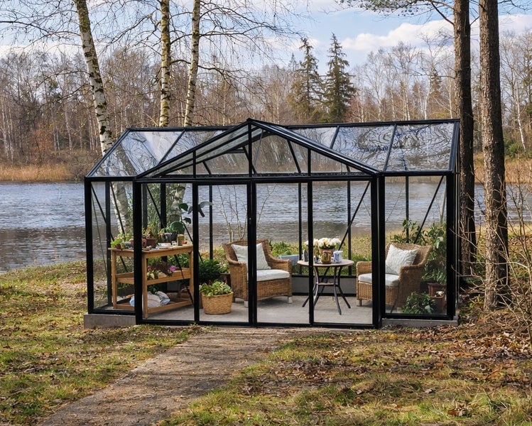 Geräumiges Gewächshaus aus Glas mit schwarzem Metallrahmen, ausgestattet mit Rattan-Sesseln und Tisch, direkt an einem See gelegen.
