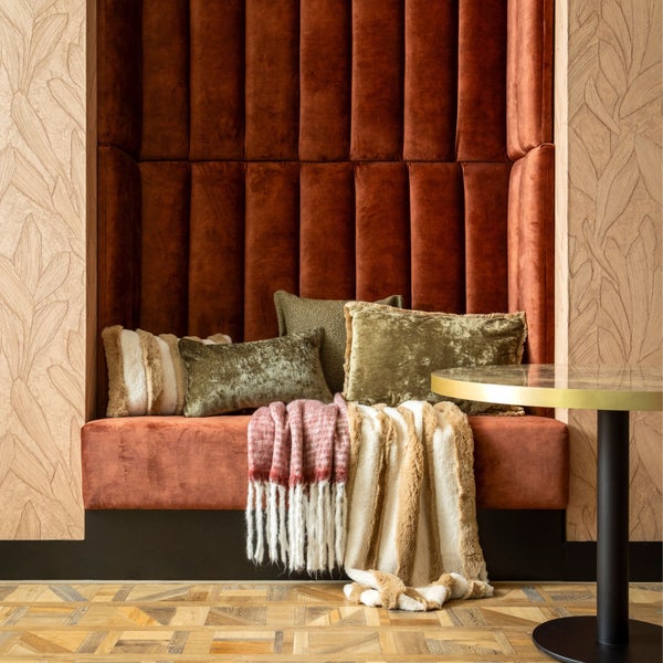 Gemütliche Sitzecke mit gepolsterter Rückwand, Kissen und Decken sowie einem kleinen Beistelltisch.