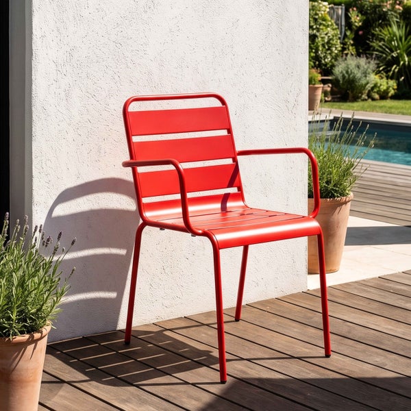 Roter Gartenstuhl aus Metall mit Armlehnen und Latten-Design auf einer Holzterrasse vor einer hellen Wand und Pflanzen.