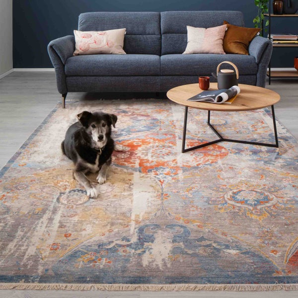 Großer Teppich im Vintage-Stil mit Ornamentmuster in einem modernen Wohnzimmer mit blauem Sofa, rundem Holztisch und einem Hund.