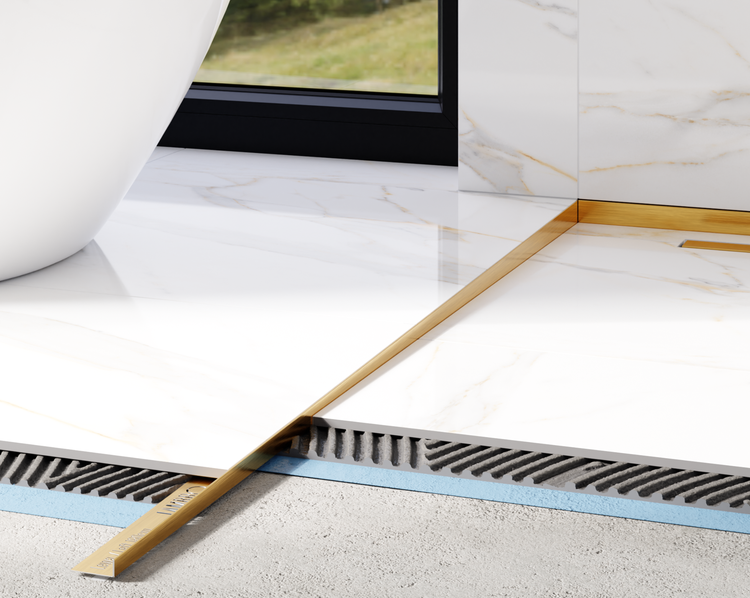 Goldfarbenes Bodenprofil zwischen Fliesen in Marmoroptik im Badezimmer, zeigt den Schichtaufbau der Bodeninstallation.