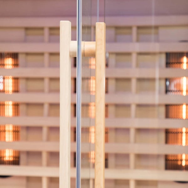 Saunatürgriff aus Holz an einer Glassauna mit Infrarotstrahlern im Hintergrund