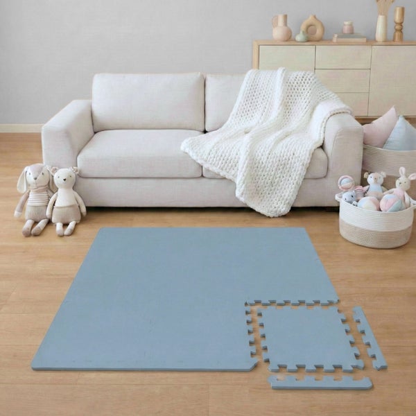 Blaue Schaumstoff-Puzzlematte in einem hellen, organisierten Wohnzimmer auf Holzboden vor einem Sofa mit Kuscheltieren.
