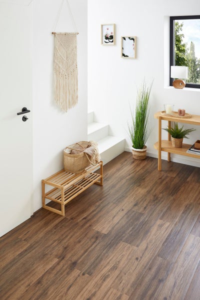 Hell gestalteter Flur mit dunklem Vinylboden in Holzoptik, Holzmöbeln und weißer Treppe.