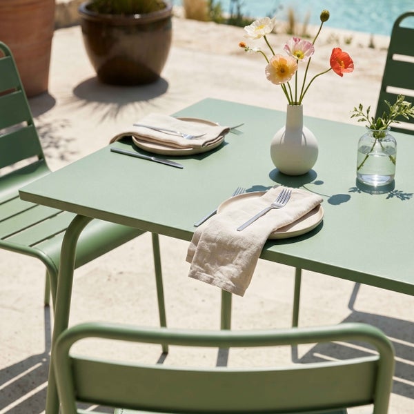 Modernes Gartenmöbel-Set aus grünem Metall auf einer hellen Terrasse mit einem quadratischen Tisch und passenden Stühlen.