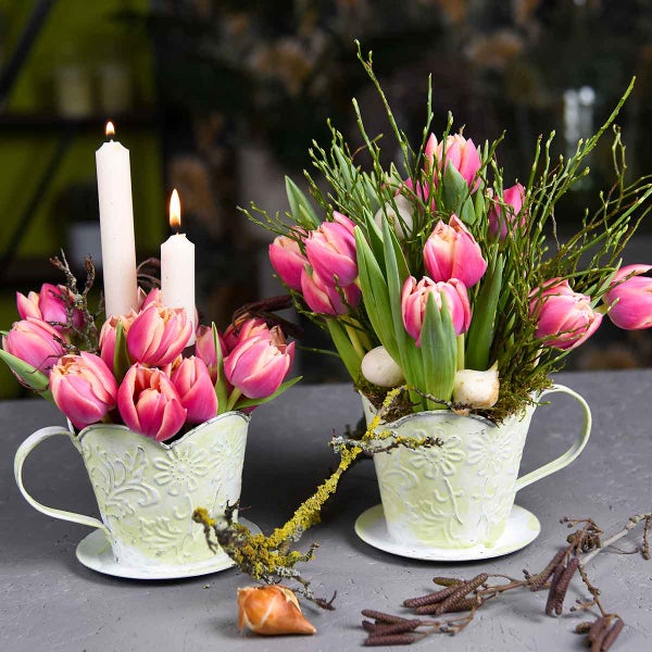 Dekorative Blumenarrangements mit Tulpen und Kerzen in Tassen als Tischdekoration.