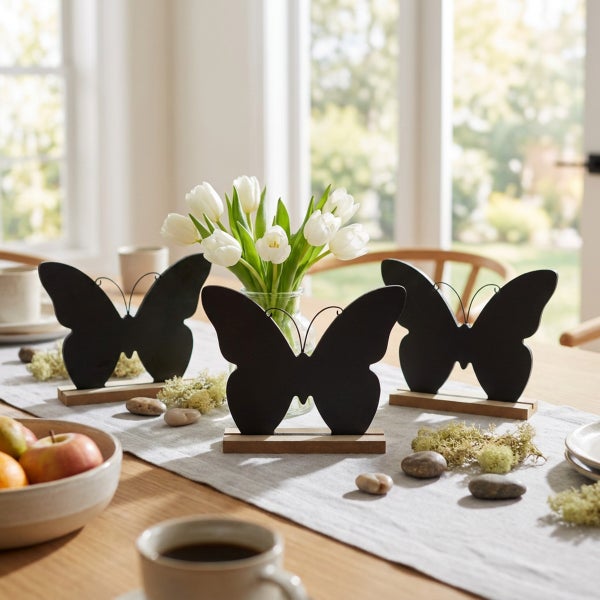 Drei Deko Schmetterlinge aus Metall mit Holzsockel auf einem Tisch mit Blumenvase und Naturdekoration als Frühlingsdekoration.