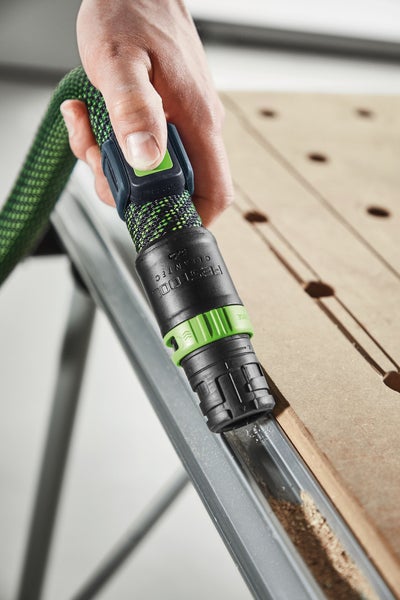 Hand führt Festool Cleantec Saugschlauch mit Anschlussmuffe zum Absaugen von Sägespänen auf einem Multifunktionstisch.