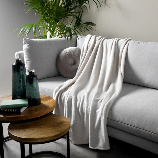 Graues Sofa mit Kuscheldecke, rundem Kissen und Beistelltisch mit Dekoration