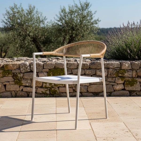 Gartenstuhl mit weißem Metallgestell und beigefarbenem Seilgeflecht an der Rückenlehne auf einer gepflasterten Terrasse vor einer Steinmauer.