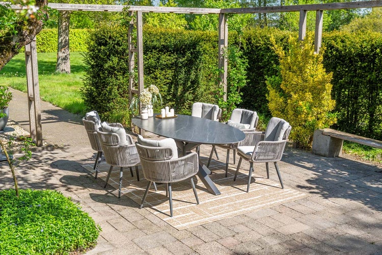 Moderne Garten Sitzgruppe mit ovalem Tisch in dunkler Steinoptik und sechs grauen Seilgeflecht Sesseln auf einer Terrasse unter einer Pergola.