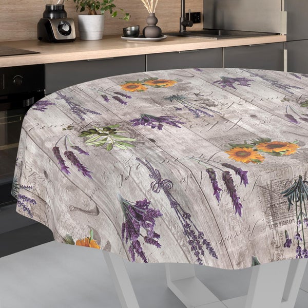 Runde Tischdecke mit Lavendel-, Sonnenblumen- und Olivenmotiven auf einem Hintergrund in Holzoptik in einer hellen, modernen Küche.