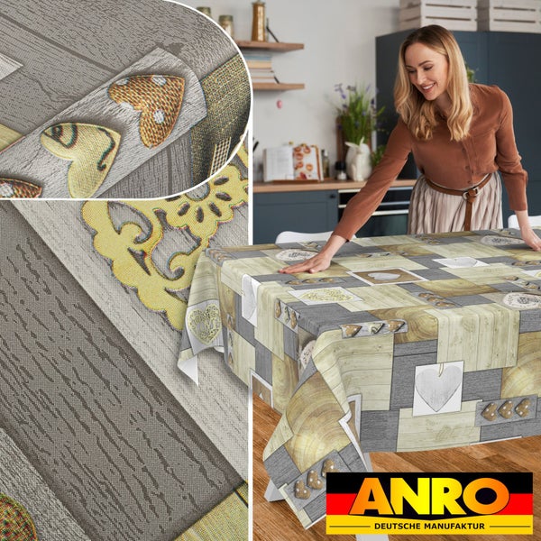 Eine Frau deckt einen Tisch mit einer ANRO Tischdecke im Patchwork-Design mit Holzoptik und Herzmotiven. Detailansicht des Gewebes. ANRO Logo.