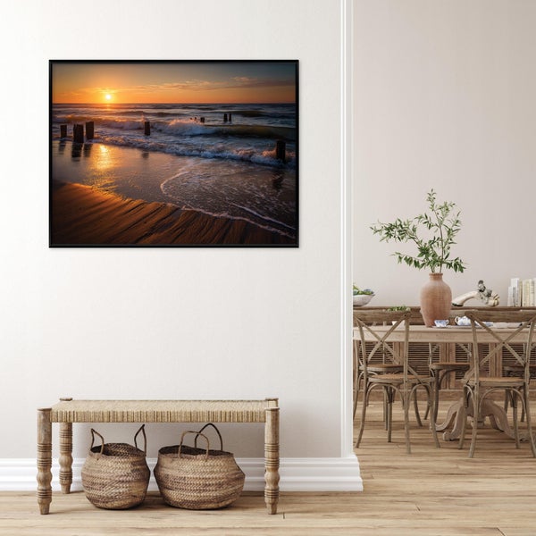 Wandbild mit Sonnenuntergang am Meer in schwarzem Rahmen, hängend über einer Sitzbank mit geflochtenen Körben in einem rustikalen Wohnbereich.