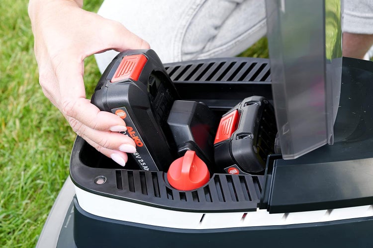 Hand setzt einen AL-KO 18 Volt 2,5 Amperestunden Akku in das Akkufach eines Rasenmähers ein.