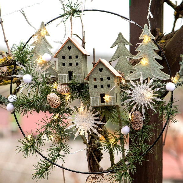 Dekorativer Metallring mit hängenden Filzhäusern, Tannenbäumen, Kiefernzweigen, Tannenzapfen und LED Lichterkette als weihnachtliche Dekoration