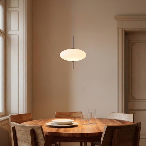 Moderne Pendelleuchte mit weißem Glasschirm über einem runden Holztisch in einem hellen Esszimmer.