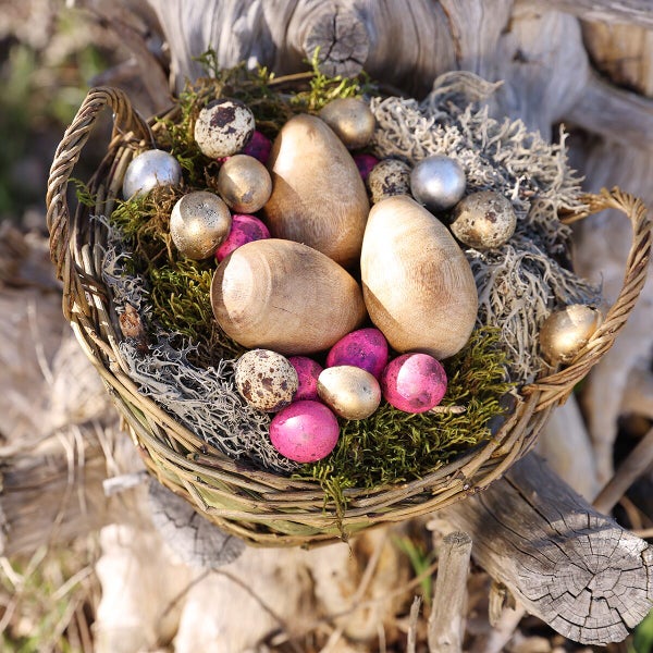 Osterkorb aus Weidengeflecht gefüllt mit Holz Ostereiern, Wachteleiern und Moos als Osterdekoration.